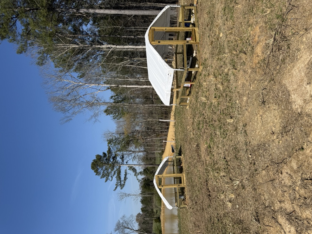 Two chicken tractors in the wide pasture with pond in the distance
